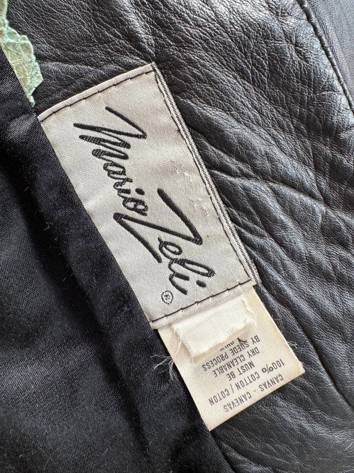 Close-up of a garment's interior label reading 'Maison Zelli' stitched on a black quilted fabric, with a cotton tag below showing material details.