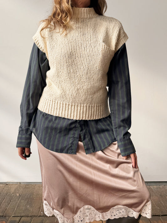 Person wearing a beige sweater over a striped shirt with a pink skirt against a plain background