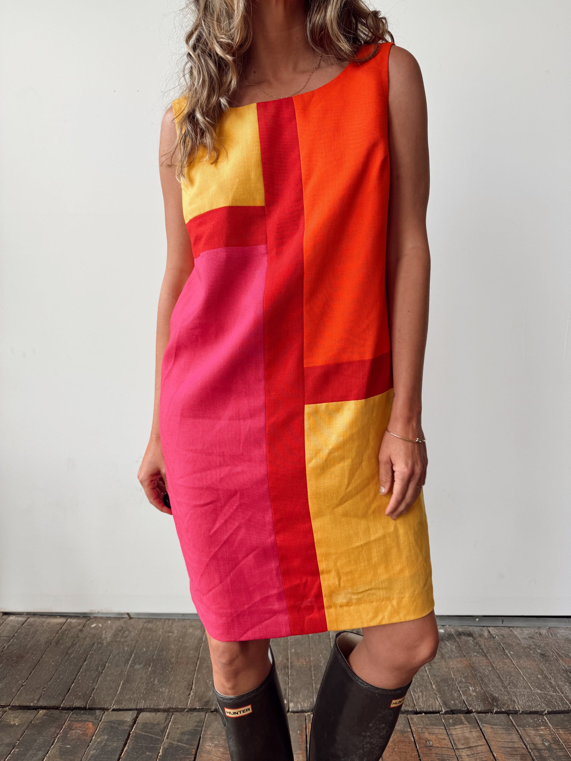 Person wearing a colorful geometric dress with rain boots on a wooden floor.