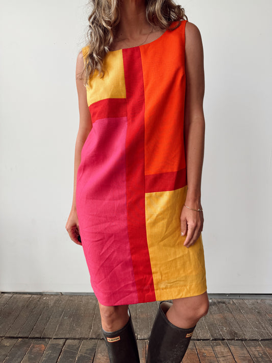 Person wearing a colorful geometric dress with rain boots on a wooden floor.