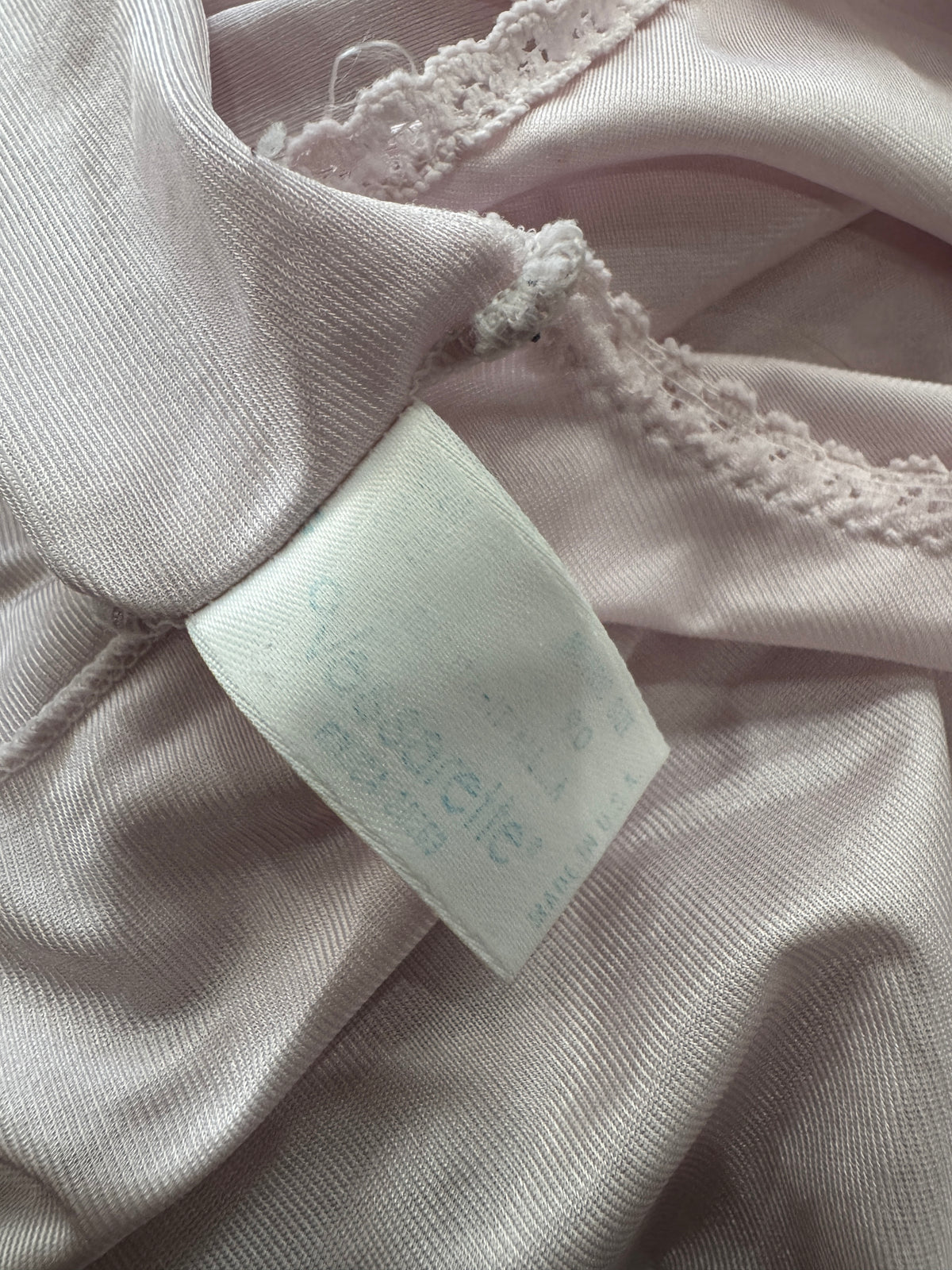 Close-up of a light pink garment with lace trim and a white fabric care label sewn inside the collar.