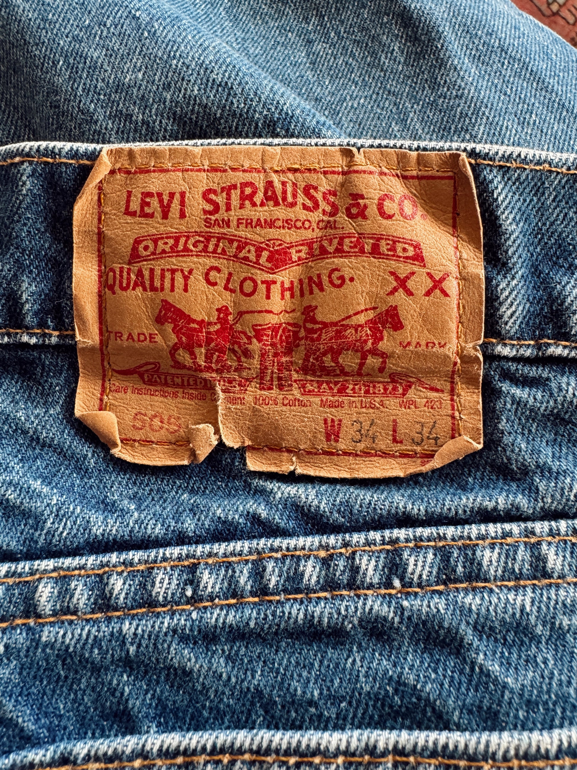 Close-up of a vintage Levi's XX denim waistband showing the original tan leather brand patch with red printed text and stitching.