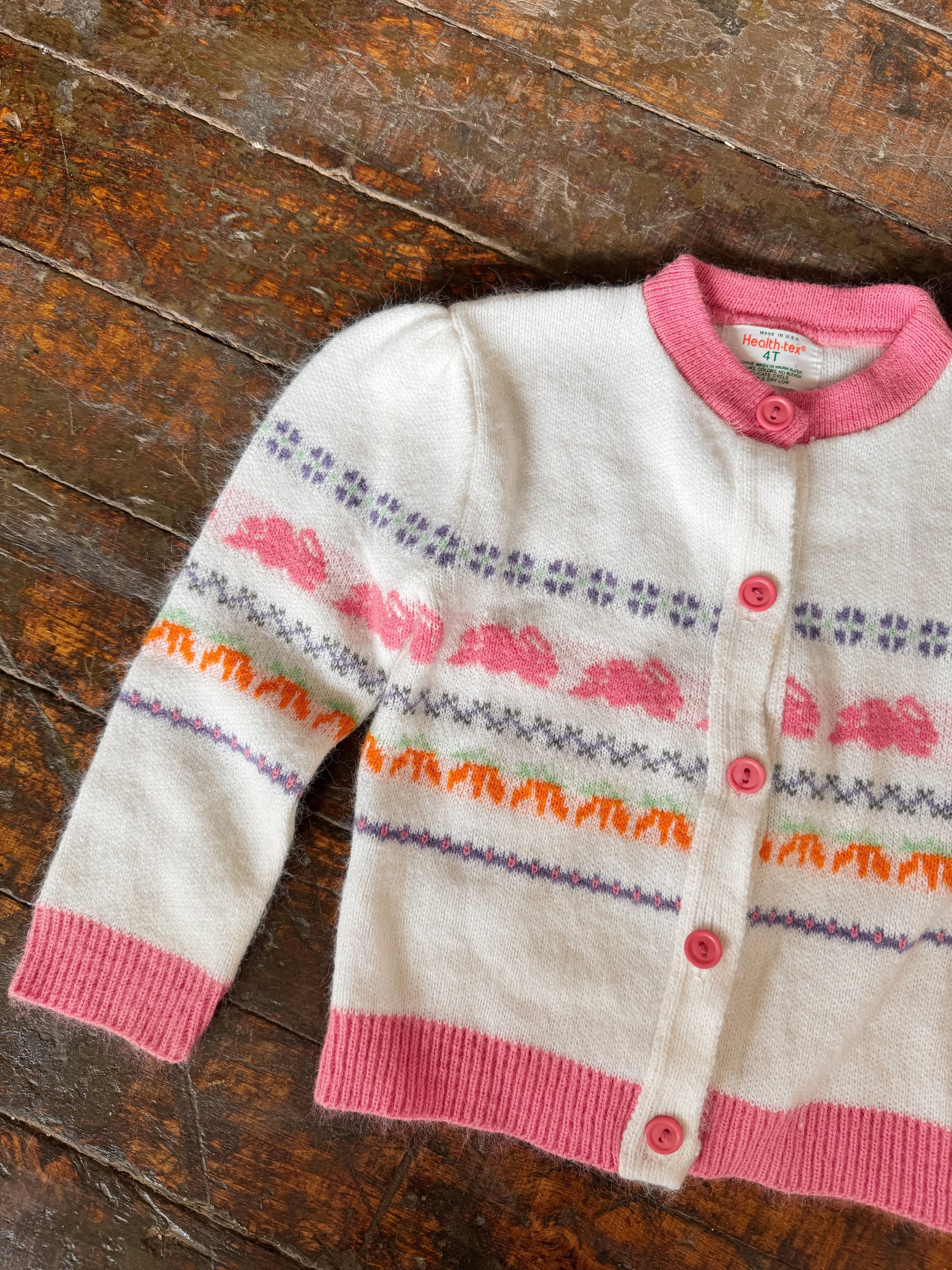 Children's cardigan with pink trim and colorful patterns on a wooden surface