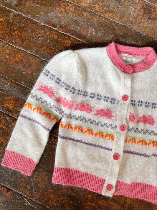 Children's cardigan with pink trim and colorful patterns on a wooden surface