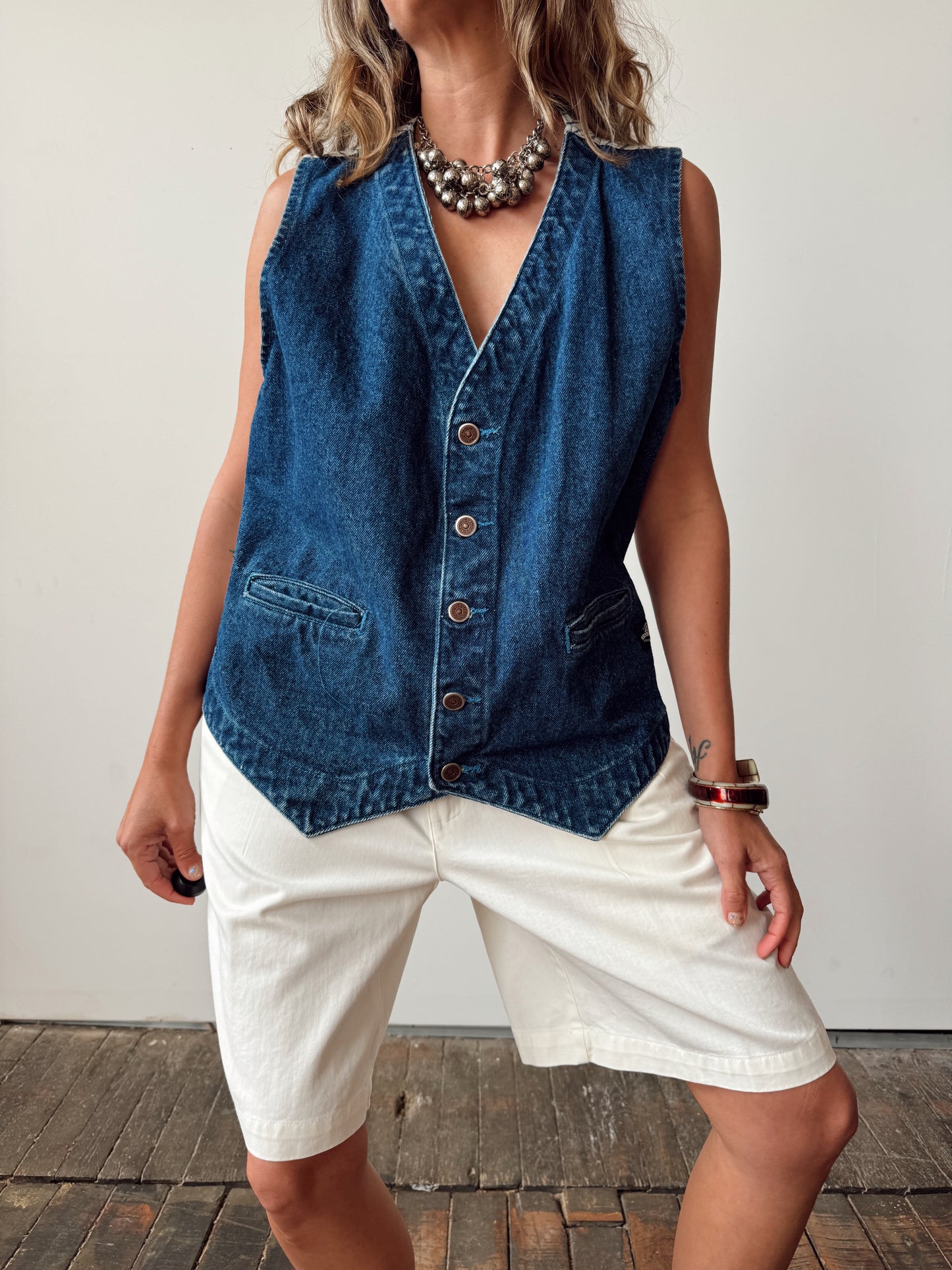 Person wearing a blue denim vest over a white shirt on a neutral background
