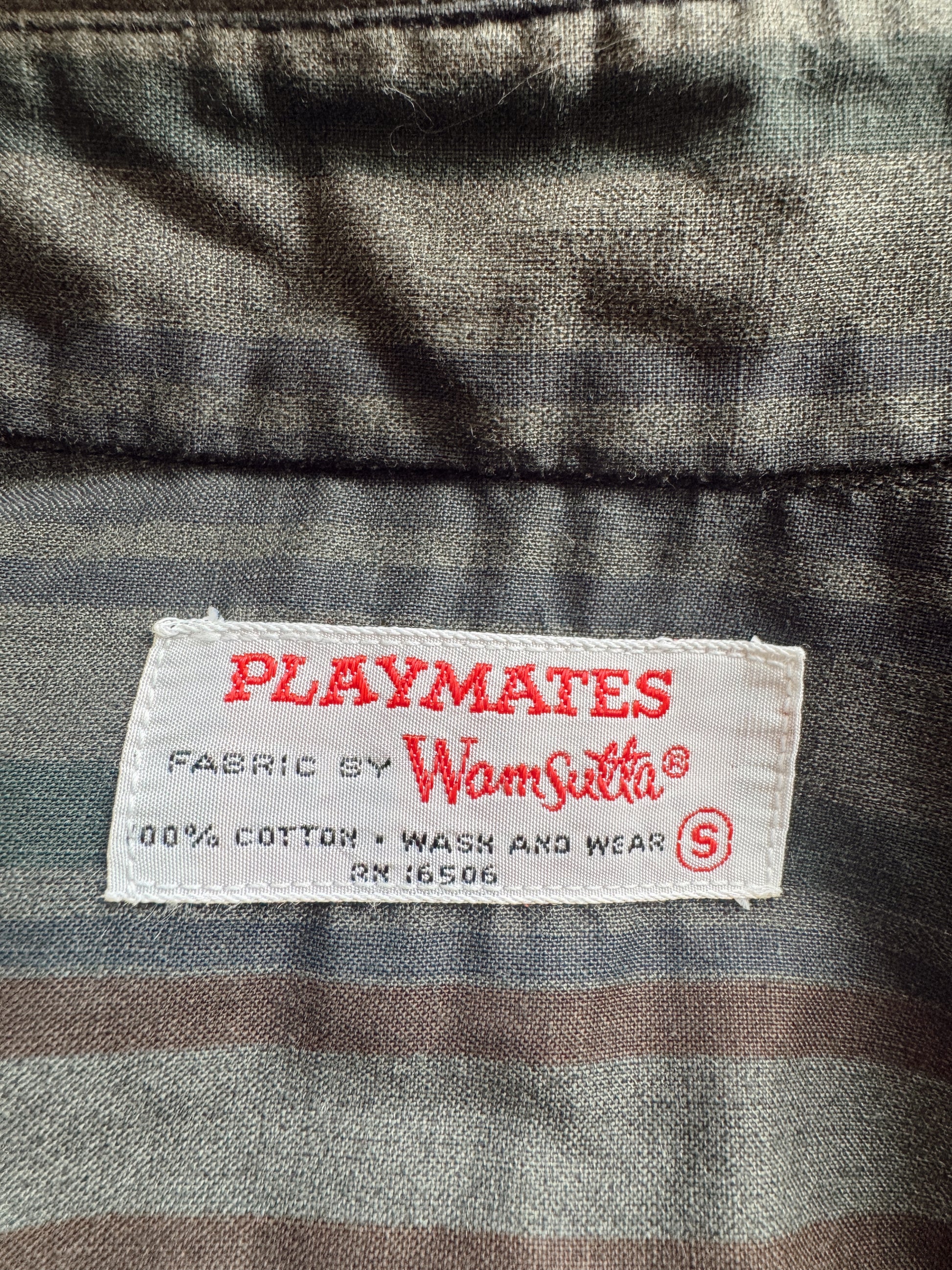 Close-up of a vintage Playmates fabric label by Wam Sutton sewn onto a gray and brown striped cotton shirt.