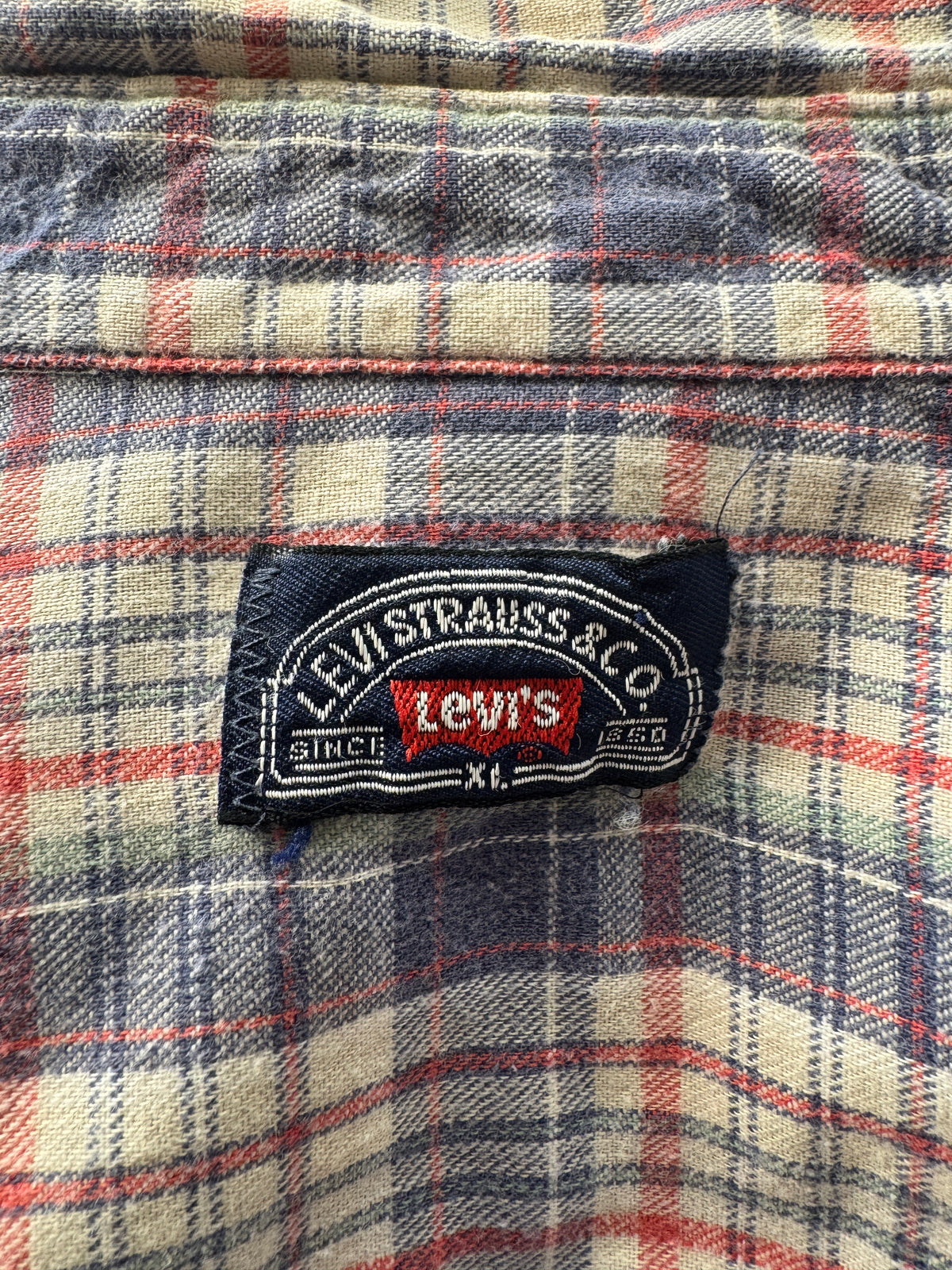 Close-up of a Levi's plaid fabric garment showing the sewn-in brand label on a cream, red, and navy plaid background.