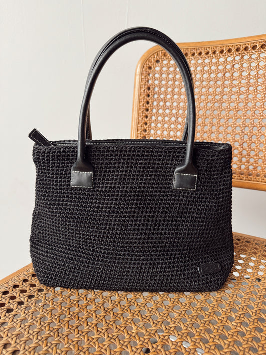 Black woven handbag with a handle on a light gray background