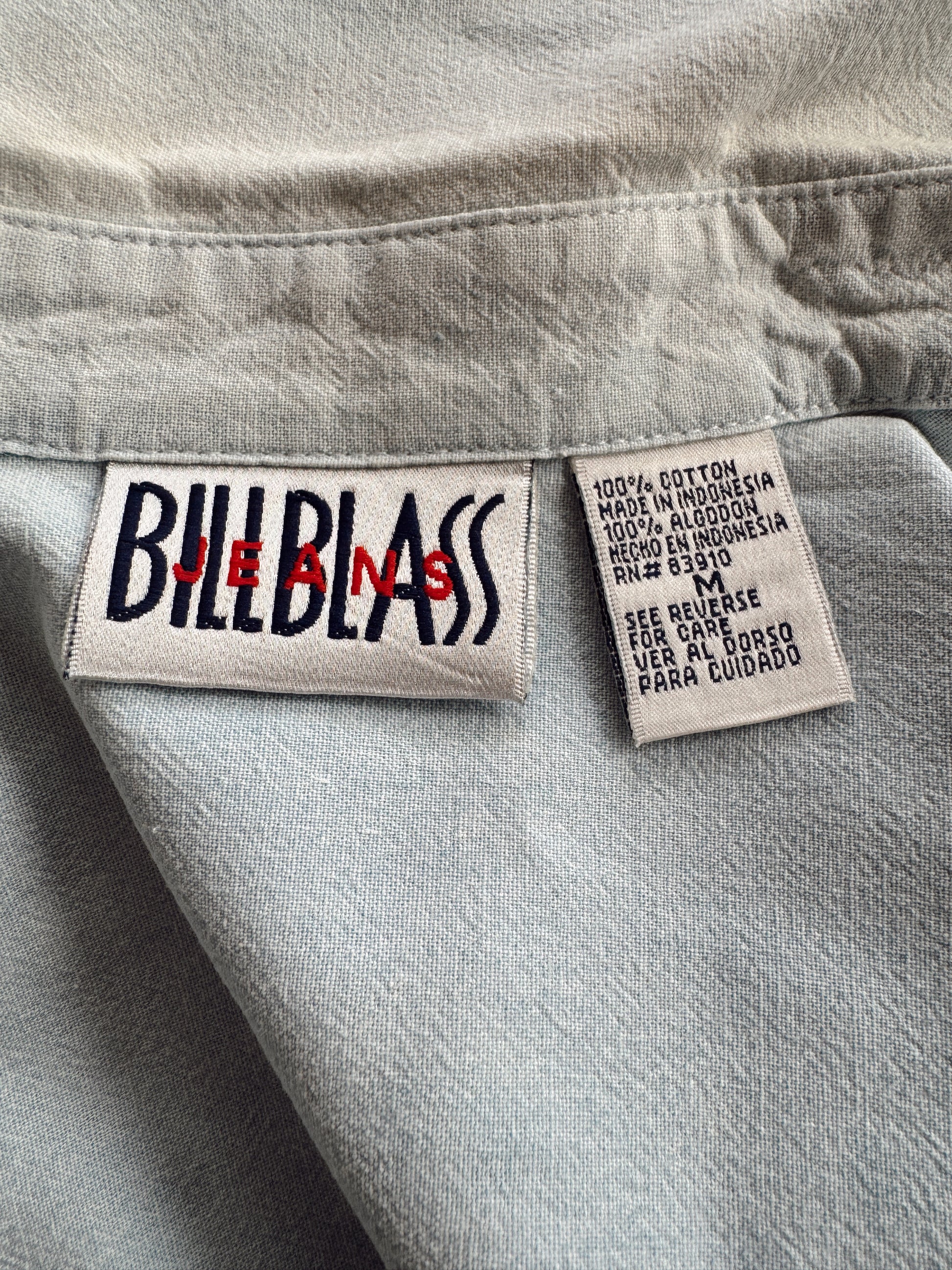 Close-up of a light gray denim garment showing two sewn-in labels: a Bill Blair Jeans logo patch on the left and a material/care label on the right.