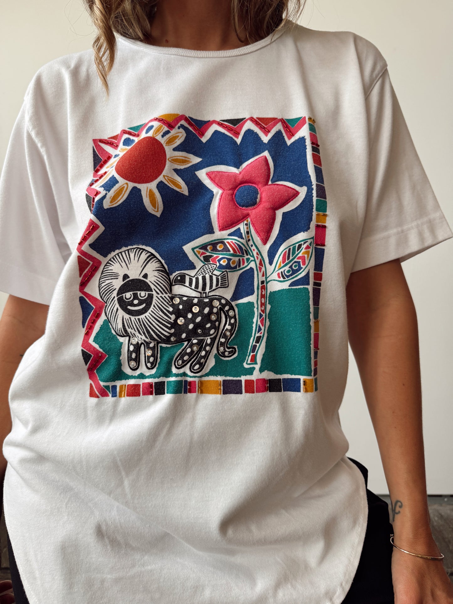 White t-shirt with a colorful graphic design featuring a lion, flowers, and geometric shapes.