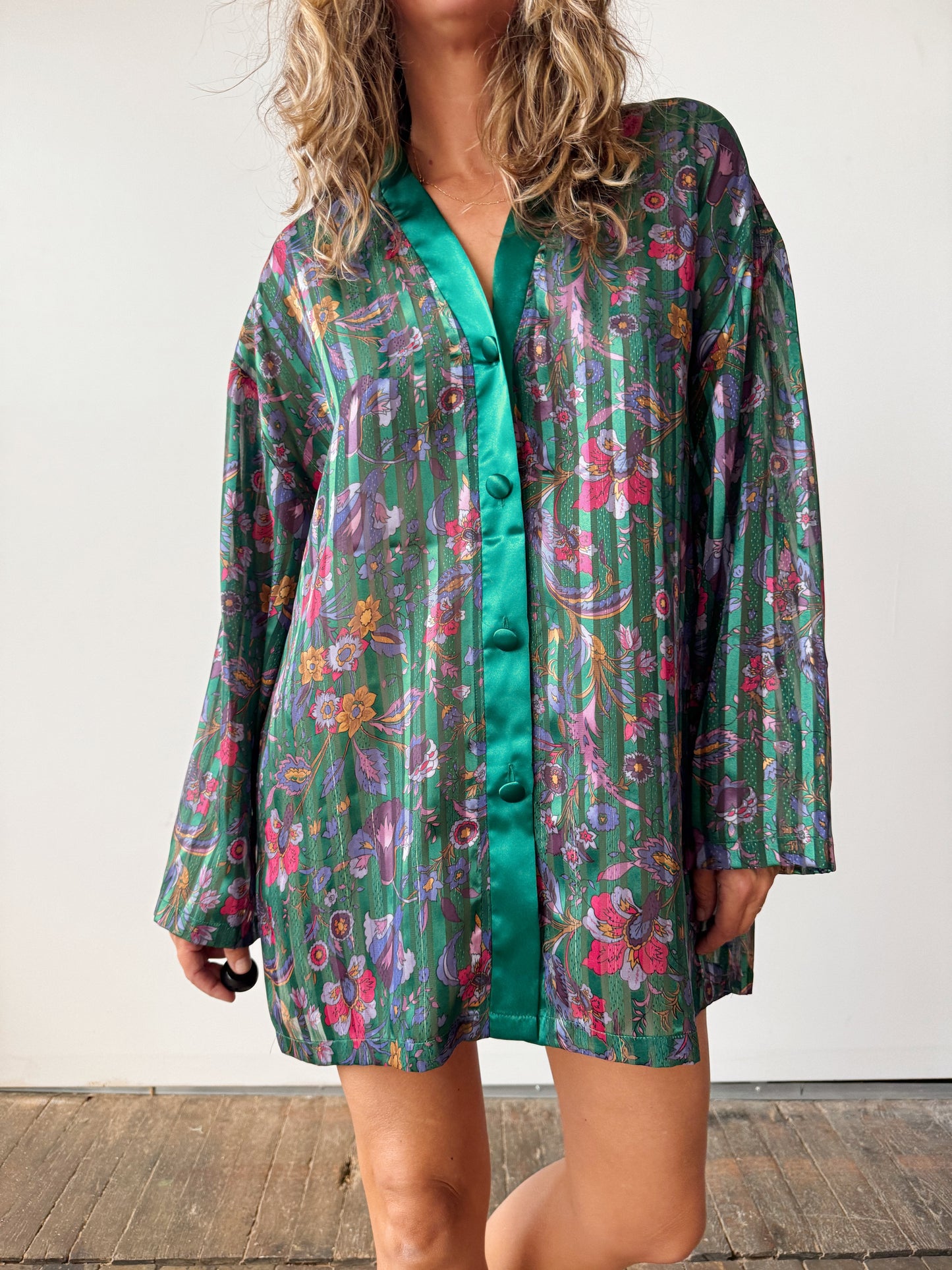 Woman wearing a floral patterned shirt over a green dress against a white background