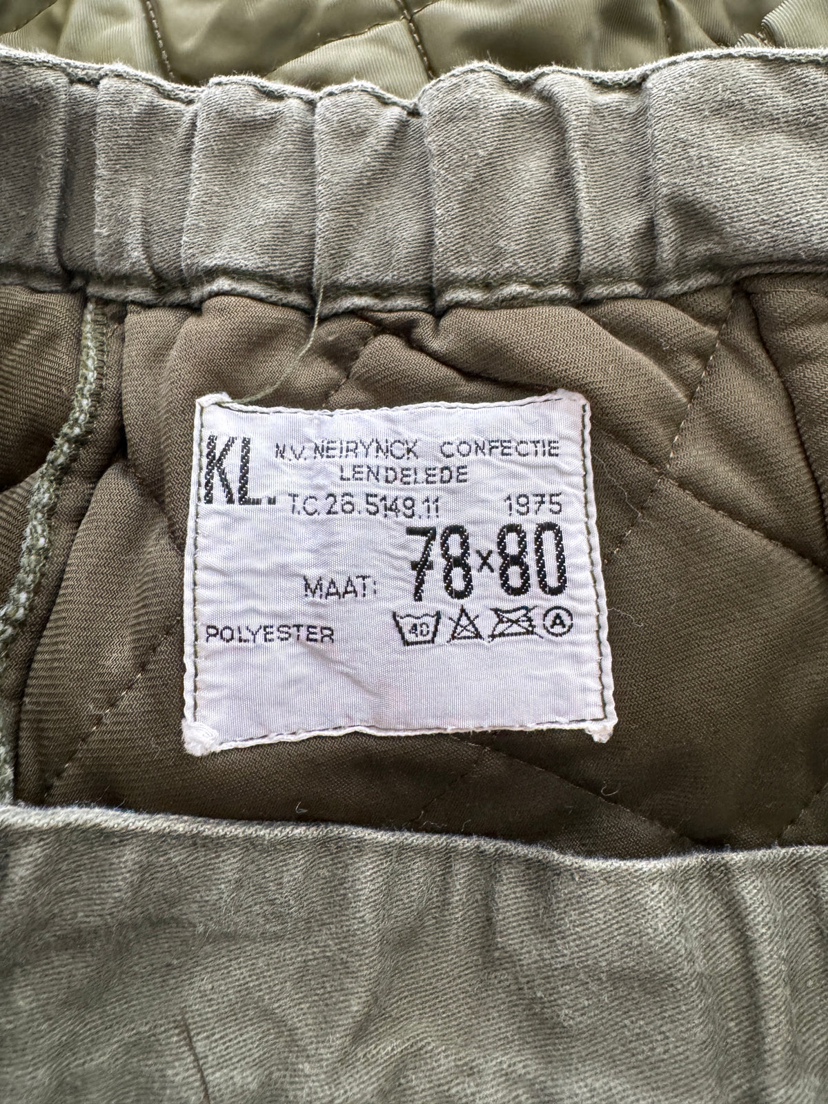 Close-up of the inner waistband and sewn-in size label of olive green quilted trousers. The white label reads 'KNV.