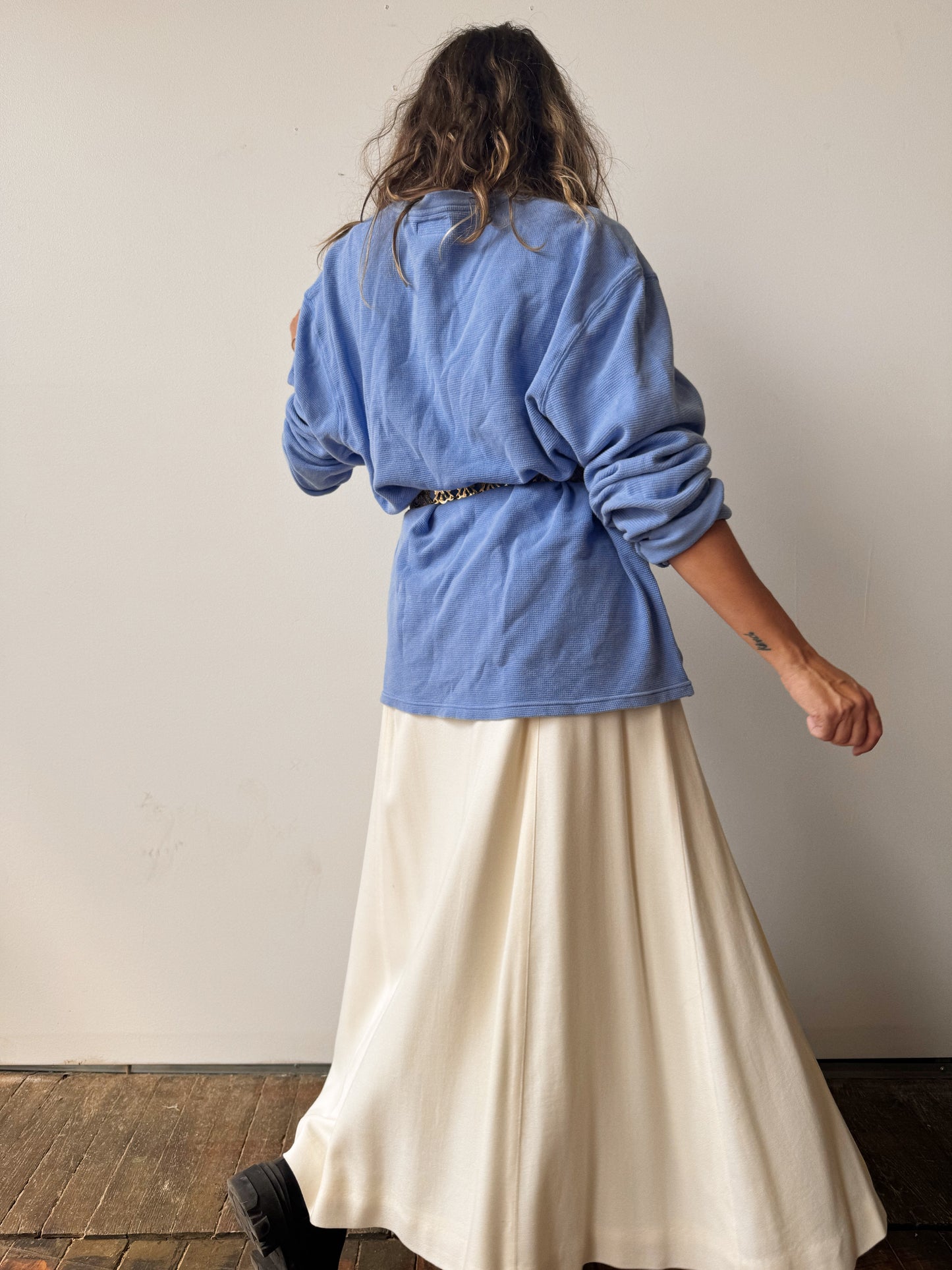 Person wearing a blue top and white skirt against a plain wall.