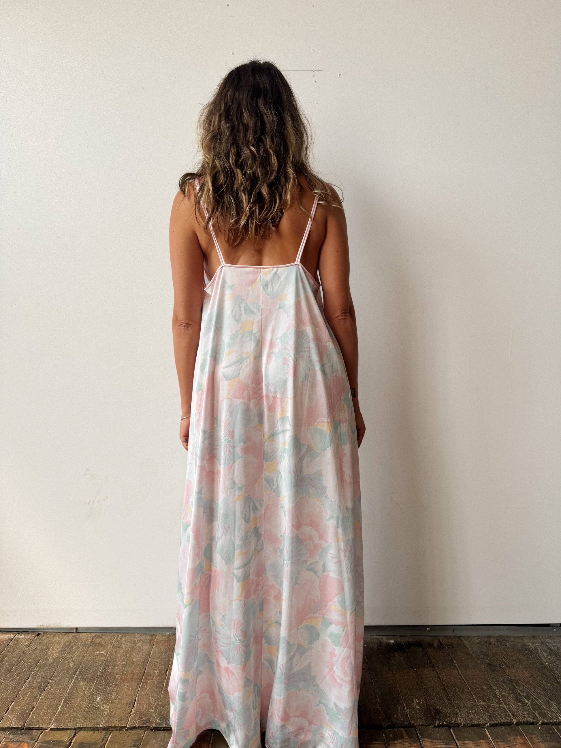 Woman wearing a floral slip dress against a white wall.