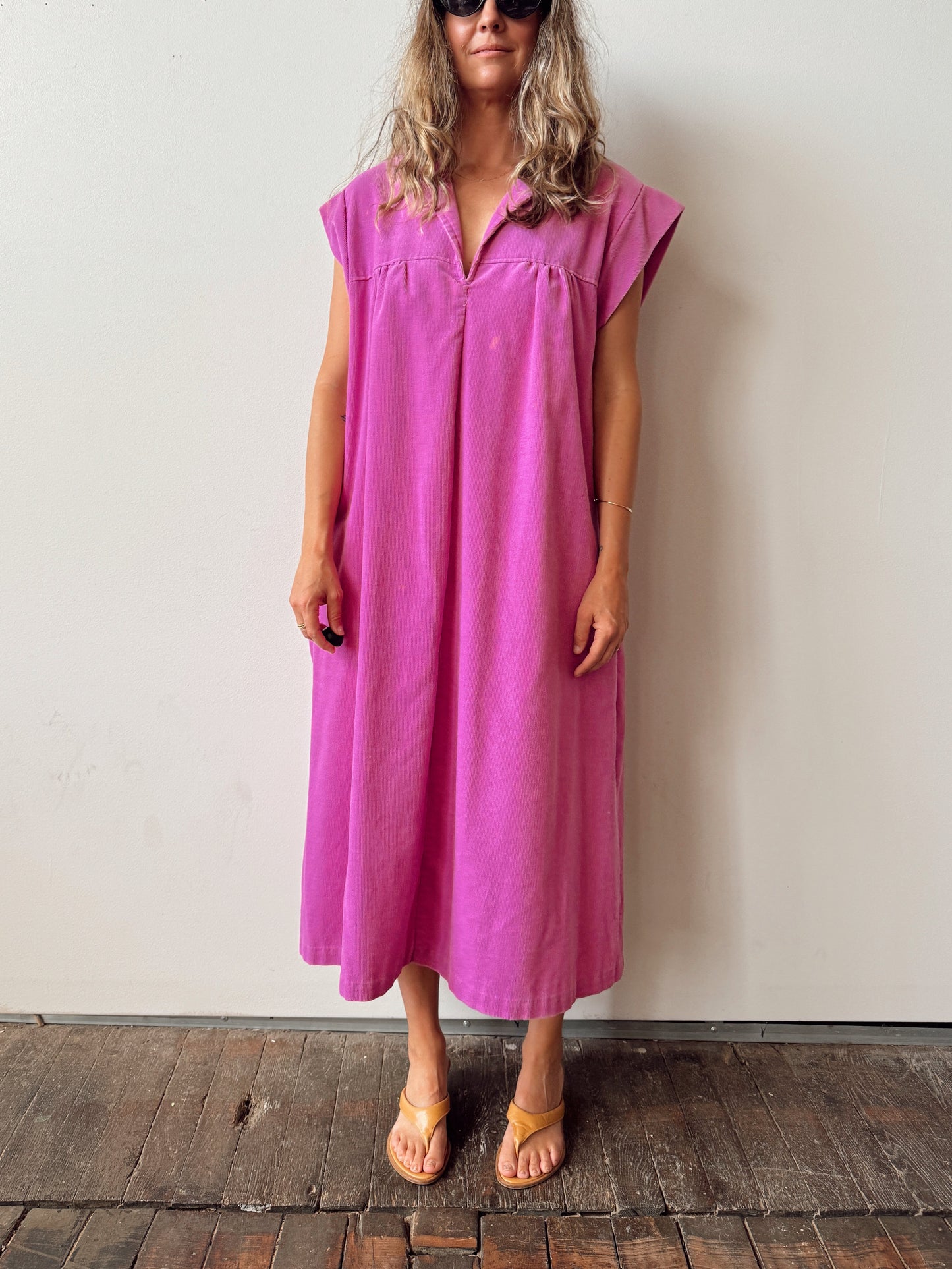 Woman wearing a pink dress standing against a plain wall.